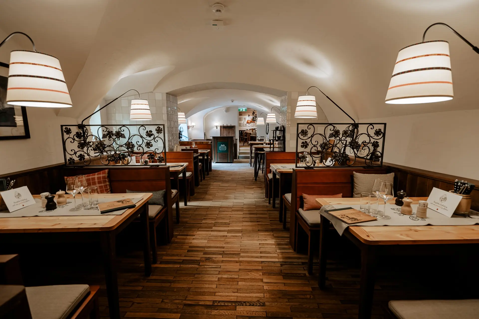 Ein gemütliches, warm beleuchtetes Restaurant mit Holzböden, Tischen und Stühlen, dekorativen Metallwänden und modernen Hängelampen, das zum Essen eingerichtet, aber derzeit leer ist.
