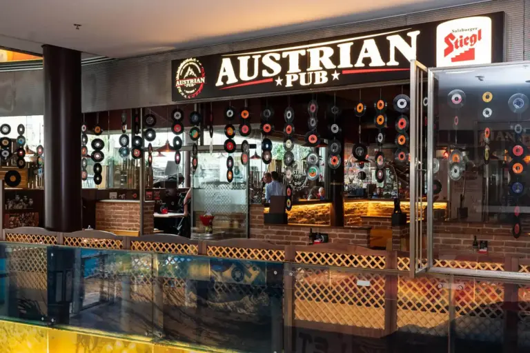 Österreichisches Pub mit großem Schild, Schallplatten an den Fenstern, Inneneinrichtung aus Holz und Ziegeln und einer Bar, hinter der Flaschen ausgestellt sind.
