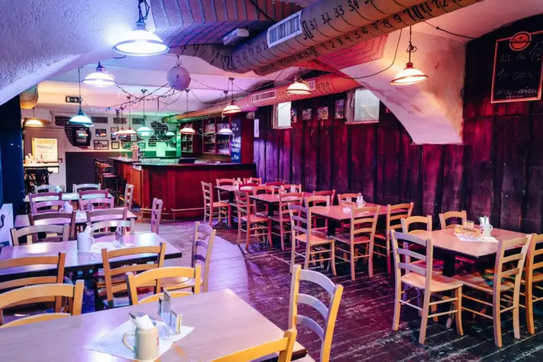 Ein gemütliches, schummriges Restaurant mit Holztischen und -stühlen, einer gewölbten Decke und bunten Hängelampen. Der Barbereich befindet sich im hinteren Teil, und die Wände sind mit dekorativen Schriftzügen und kleinen gerahmten Bildern geschmückt.