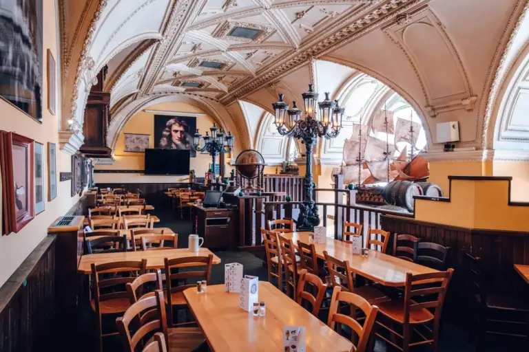 Ein geräumiges, verziertes Restaurant mit gewölbten Decken, Holztischen und -stühlen, alten Kronleuchtern und maritimem Dekor, darunter ein großes Modellschiff und ein Globus in der Nähe der Fenster.
