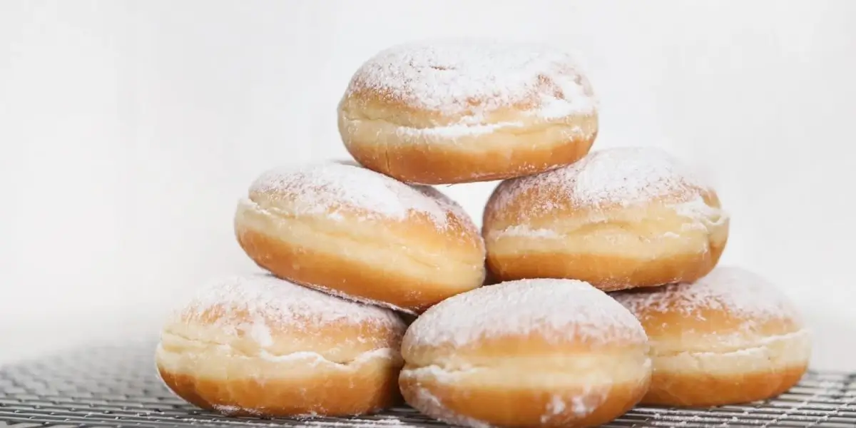 Ein Stapel von sechs runden Puderzucker-Donuts - perfekt für jedes Faschingsrezept - in einer Pyramide auf einem Kühlgestell vor weißem Hintergrund angeordnet.