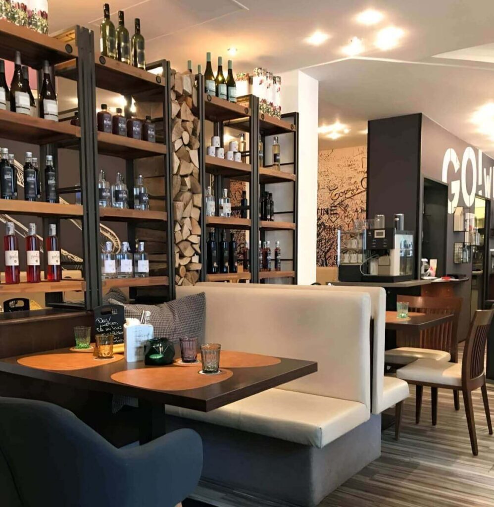 Ein gemütliches, modernes Restaurant mit gepolsterten Stühlen, Holztischen und Regalen mit Weinflaschen und gestapeltem Brennholz. Die warme Beleuchtung schafft eine einladende Atmosphäre - perfekt, wenn man den Partyraum mieten Wien möchte.