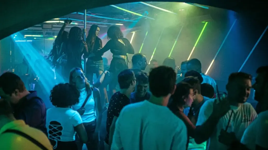 Eine belebte Nachtclubszene in einem der Clubs in Wien, mit bunten Neonlichtern, tanzenden Menschen auf einer erhöhten Plattform und geselligen Gruppen - die perfekte Inspiration, wenn Sie eine Geburtstagsparty in einer lebhaften, energiegeladenen Atmosphäre planen möchten.