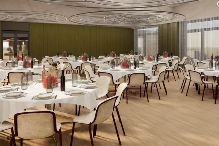 Ein moderner Bankettsaal mit runden Tischen, die mit Flaschen, Gläsern und Blumensträußen dekoriert sind. Cremefarbene Stühle umgeben die Tische, und große Fenster lassen natürliches Licht herein.