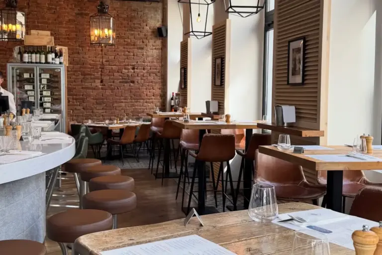Ein gemütliches, modernes Restaurant mit Backsteinwänden, Holztischen, braunen Ledersesseln, großen Fenstern und Hängelampen - Pacos einladender Raum bietet ordentlich gedeckte Tische für die Gäste.