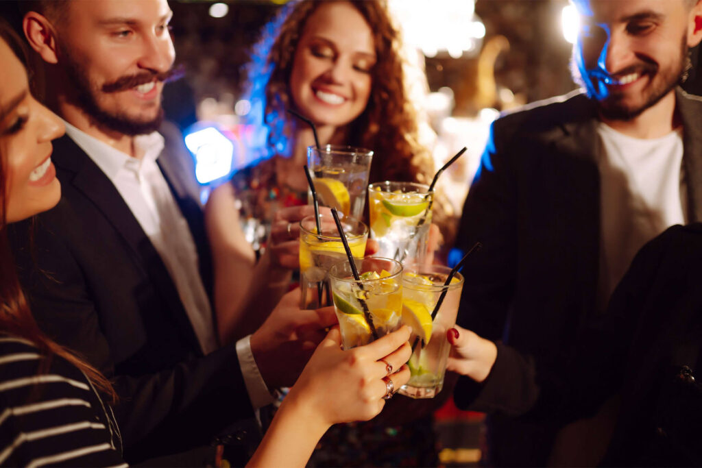 Eine Gruppe von Menschen, die lächelnd die mit Getränken und Zitronenscheiben gefüllten Gläser erheben und gemeinsam auf eine lebhafte Veranstaltung in einer beliebten Partylocation in Wien anstoßen.