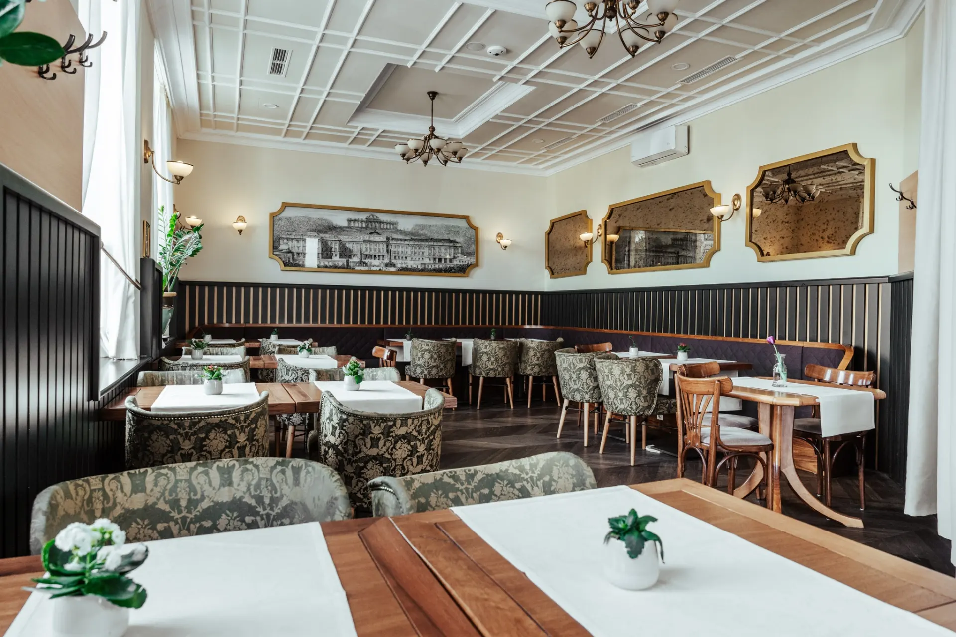 Tafelspitz Ein helles, elegantes Restaurant mit weiß gedeckten Tischen, gemusterten Stühlen, Topfpflanzen und großen Spiegeln an cremefarbenen und dunkel getäfelten Wänden. Der Raum ist mit hohen Decken und Kronleuchtern ausgestattet.