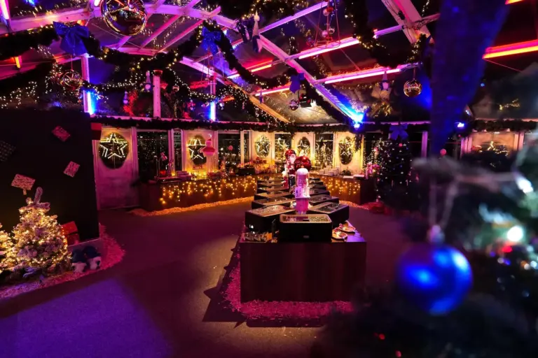 Ein festlich geschmückter Innenraum mit Weihnachtsbäumen, Girlanden, Lichterketten, Ornamenten und heller, farbenfroher Beleuchtung, die eine warme und einladende Weihnachtsatmosphäre schafft.