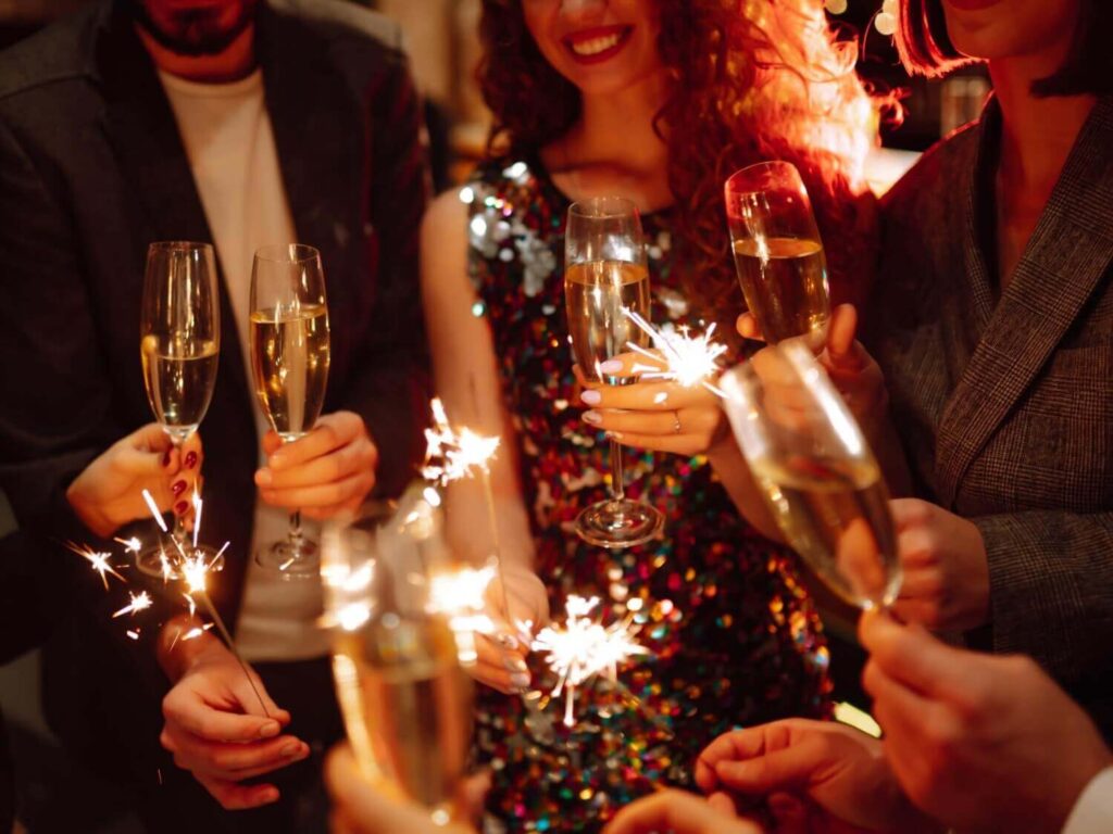 Eine Gruppe von Menschen feiert mit Wunderkerzen und Sektgläsern bei einer Weihnachtsfeier in Wien. Festlich gekleidet - und einer in einem glitzernden Kleid - ist die fröhliche Atmosphäre lebendig und unvergesslich.